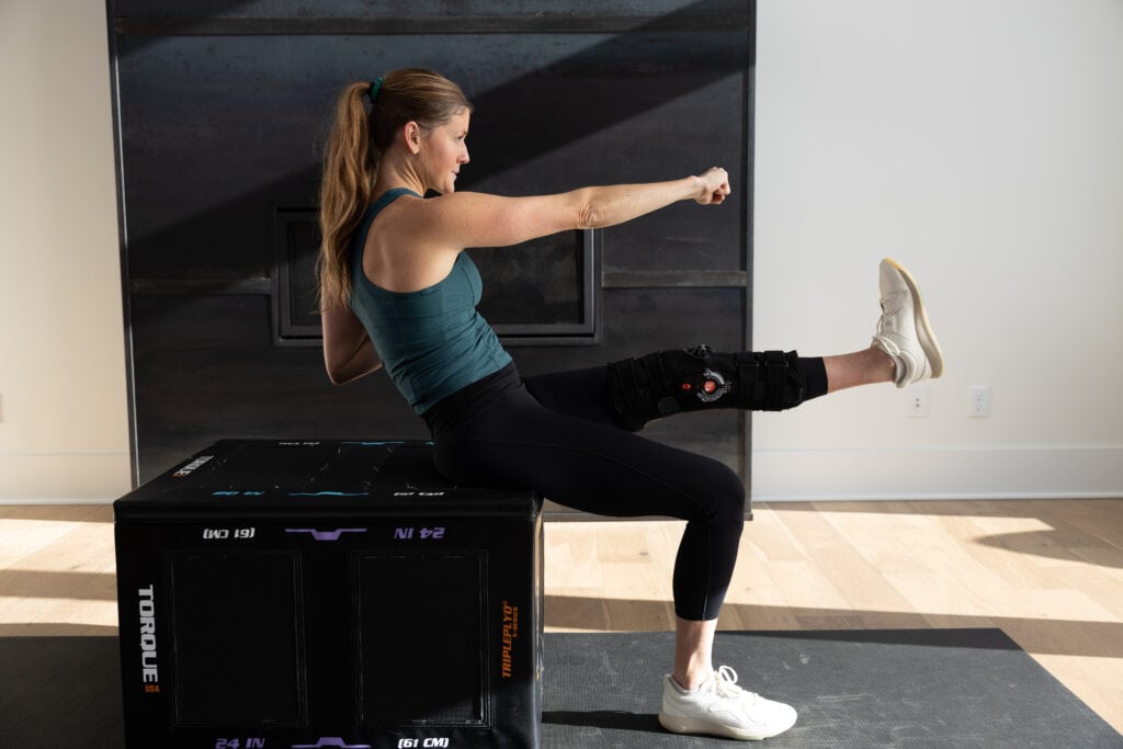 Women sitting on a workout box during a cardio chair workout doing a punch and kick move. 