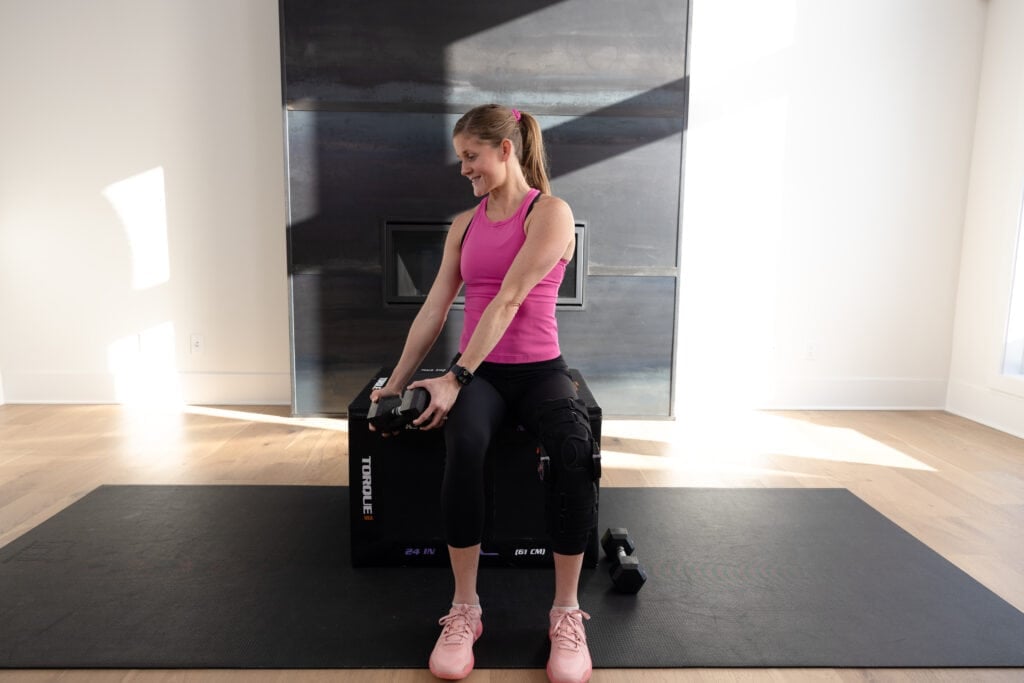 Women in pink sitting on a box doing a seated ab workout.
