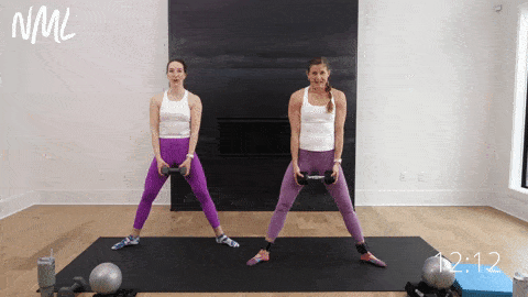 two women performing a sumo squat and dumbbell front raise with an alternating heel lift in a pilates workout at home
