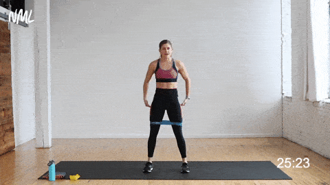 Women in a aow squat hold with feet shoulder width distance apart at the bottom of the squat hold she is doing an abduction during a resistance band exercises for legs. 