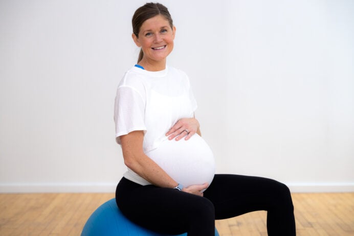 pregnant woman sitting on pregnancy exercise ball with hands resting on her baby bump.