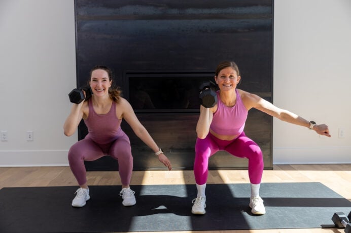 two women performing an uneven dumbbell squat hold in a full body EMOM workout