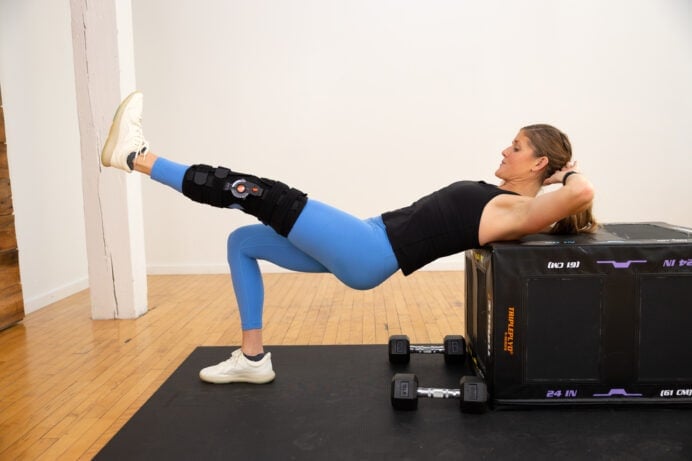 Women working out with a knee injury doing a one leg glute bridge with shoulders on a box.