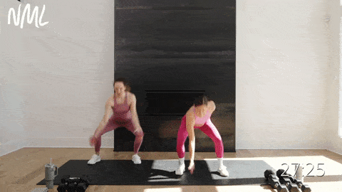 two women performing squat jacks in a full body EMOM workout at home
