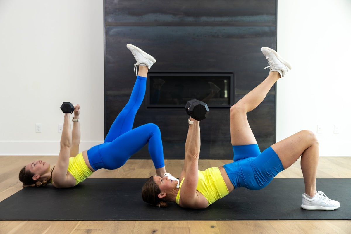 two women performing a single leg glute bridge and single arm dumbbell chest press in a full body push workout