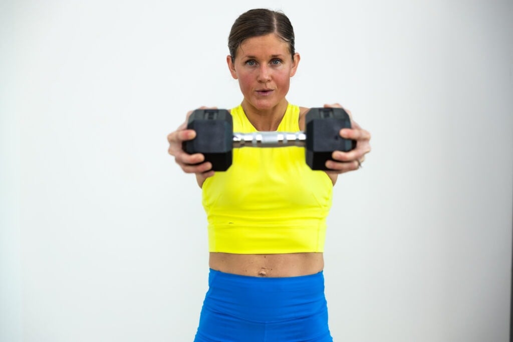 woman performing a dumbbell press out in a full body push workout
