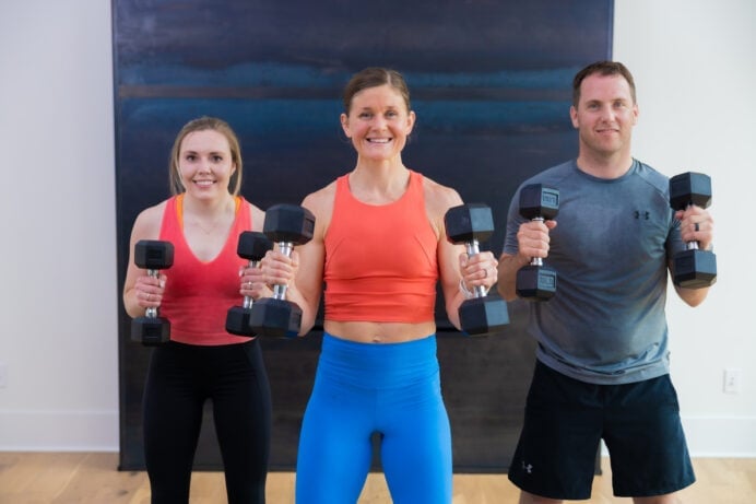 Three people standing performing a bicep curl with dumbbells as part of cardio and strength training workout