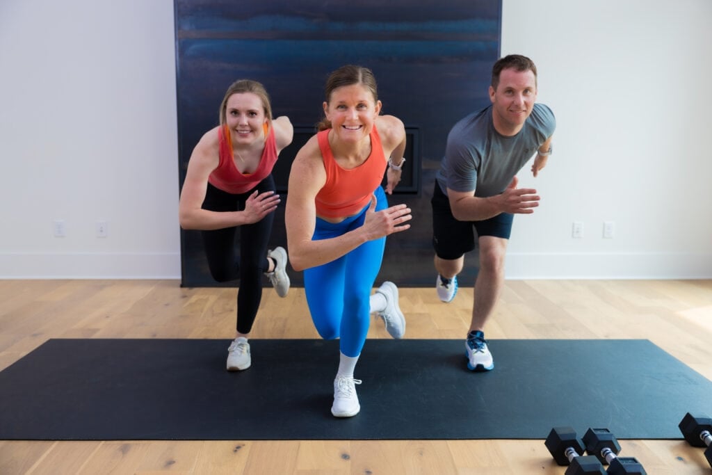 three people standing on a black mat performing a cardio exercise as part of cardio and strength workout