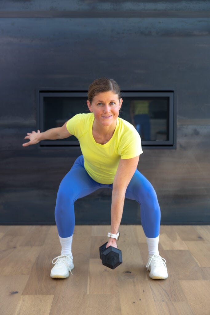 Woman performing a low squat with a dumbbell as part of lower body workout with dumbbells