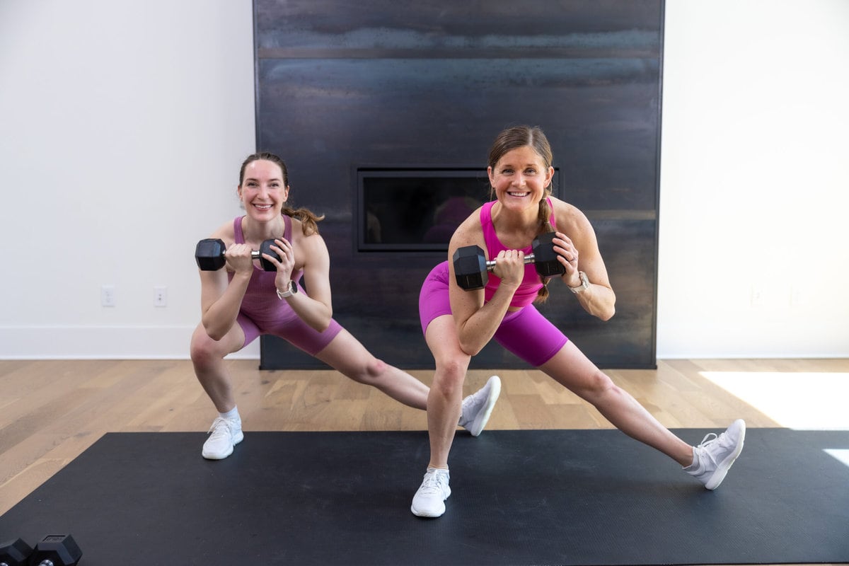 two women performing a lateral lunge hold with a dumbbell in a leg workout at home