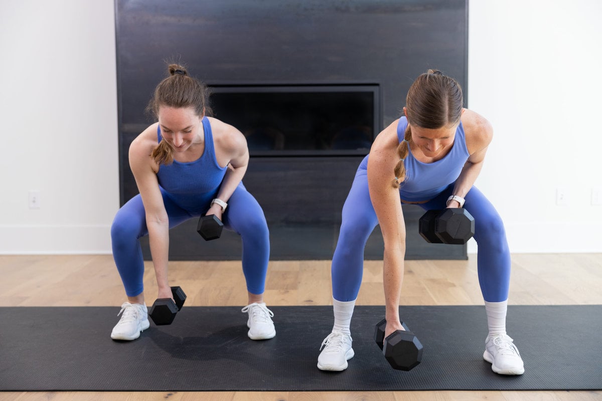 two women performing a low squat hold and dumbbell back row in a full body strength workout