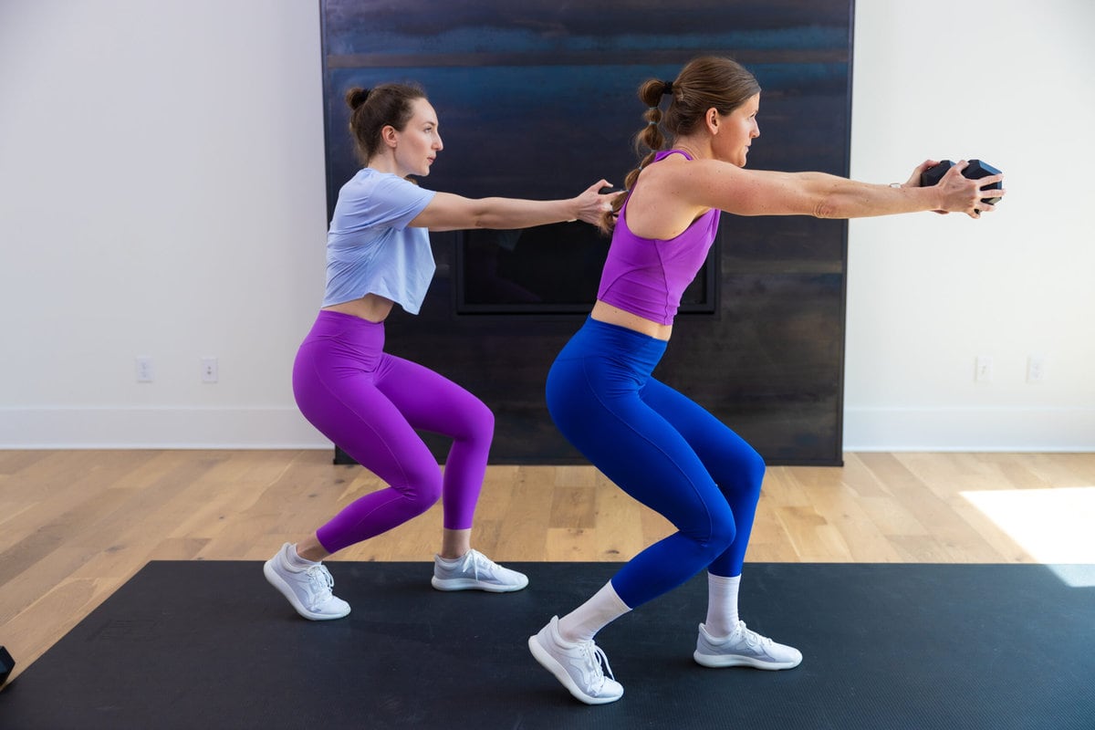 two women performing a lateral shuffle and dumbbell press in a push workout at home