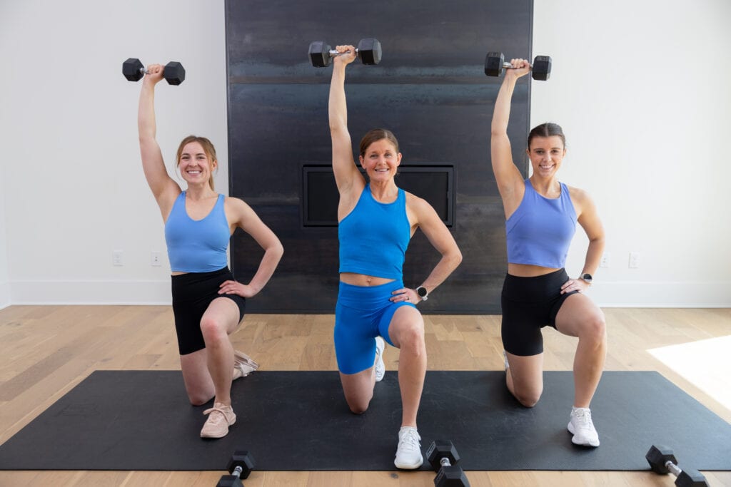 three women performing a kneeling single arm shoulder press in an arm workout at home