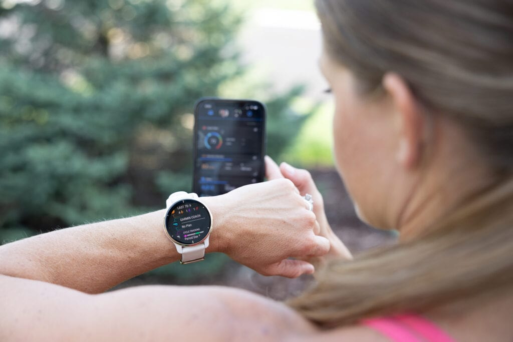 Woman wearing a Garmin Venu 2 Plus showing the Garmin coach along side the Garmin Connect app on phone. 