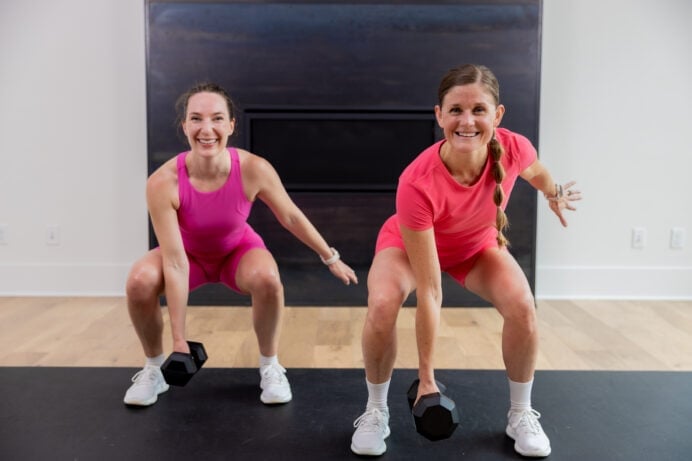 two women performing a low squat hold and single arm dumbbell hold in a full body hiit workout