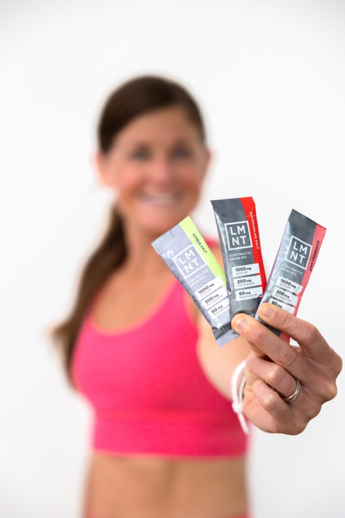 women holding out three flavors of the LMNT electrolyte packets. Flavors: watermelon salt, raspberry salt and citrus salt.