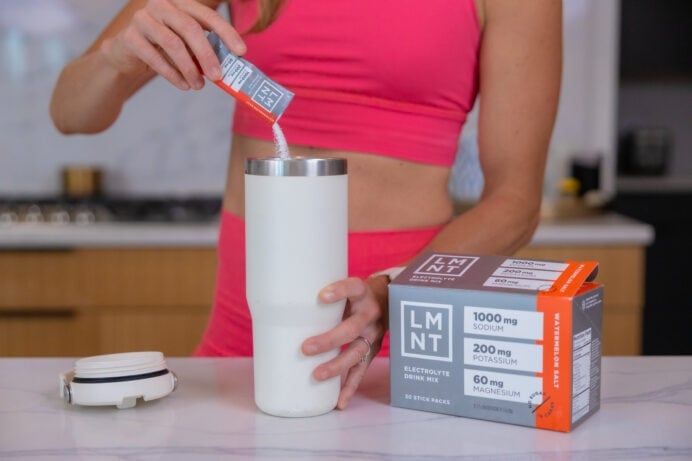 Women pour LMNT electrolyte into a water bottle in her kitchen.