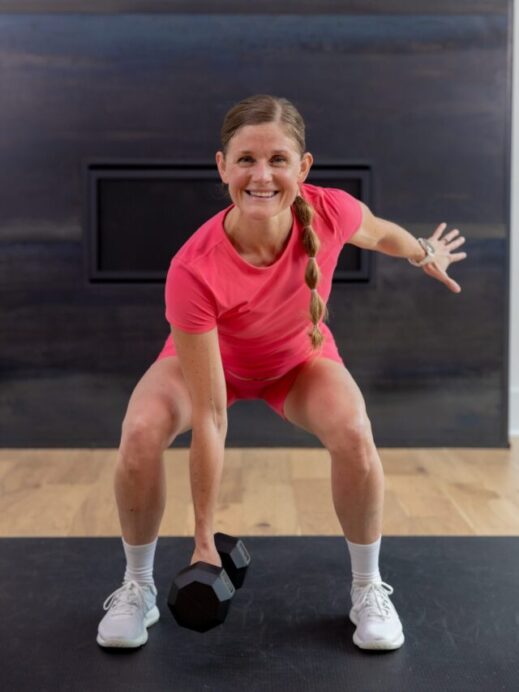 woman performing a low squat hold and single arm dumbbell hold in a full body hiit workout