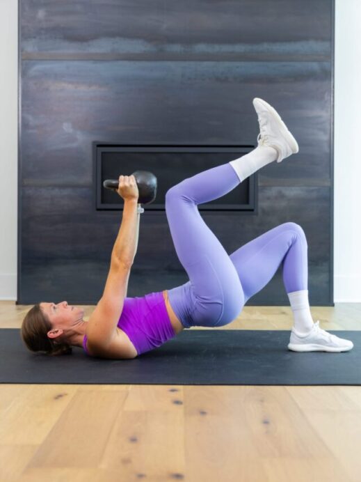 woman performing an overhead pull and glute bridge march in a kettlebell ab workout
