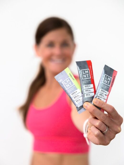 women holding out three flavors of the LMNT electrolyte packets. Flavors: watermelon salt, raspberry salt and citrus salt.