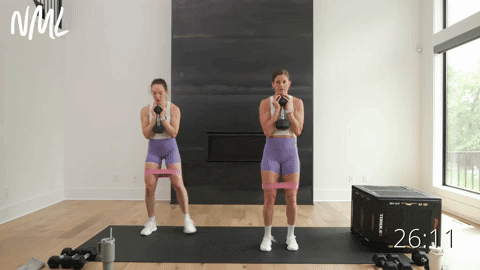 two women performing a goblet squat jack with dumbbells in a leg workout