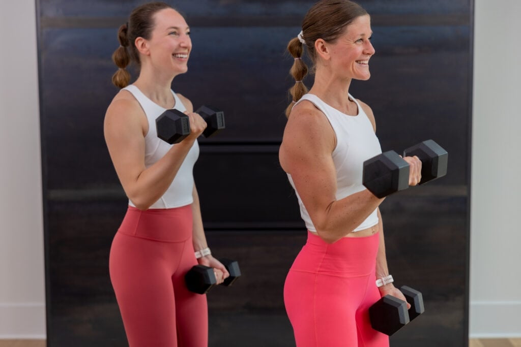 two women performing a single arm bicep curl hold in an arm workout with dumbbells