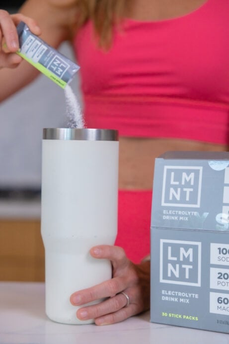 woman pouring LMNT electrolyte drink mix into a water bottle