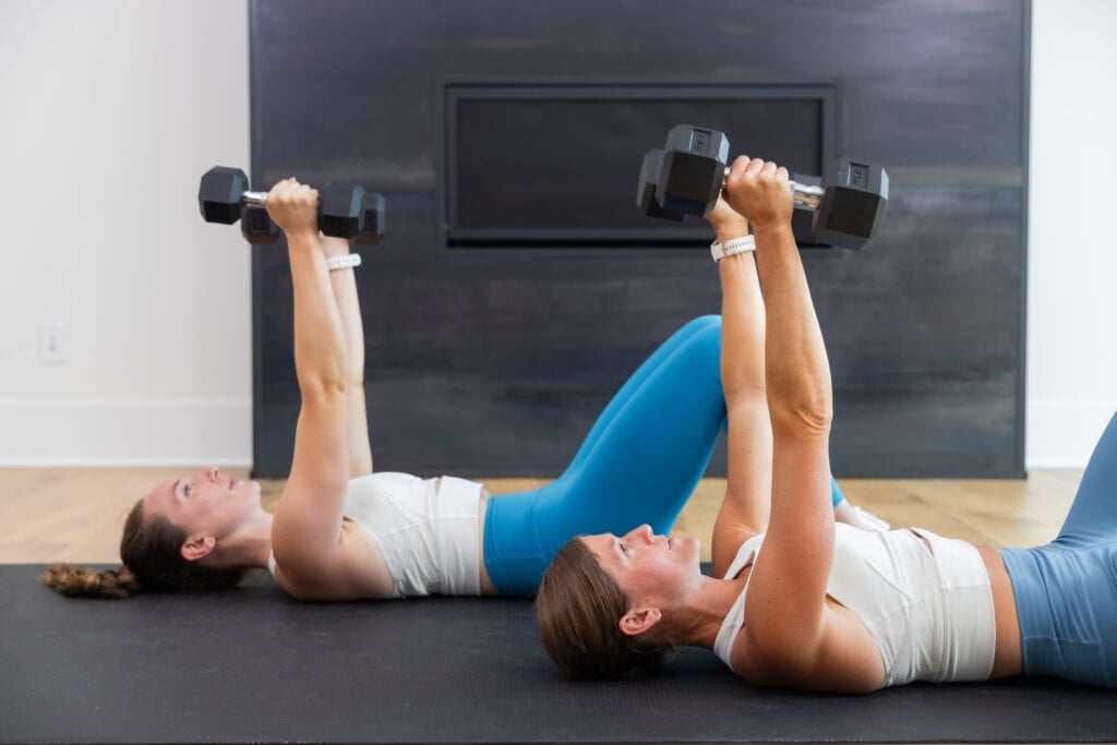 two women performing a narrow floor press in a tricep workout for women