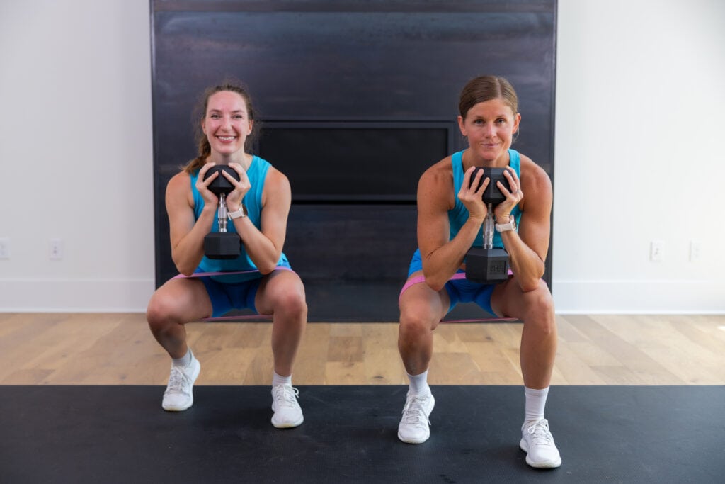 two women performing an 80/20 squat in a squat workout at home with dumbbells