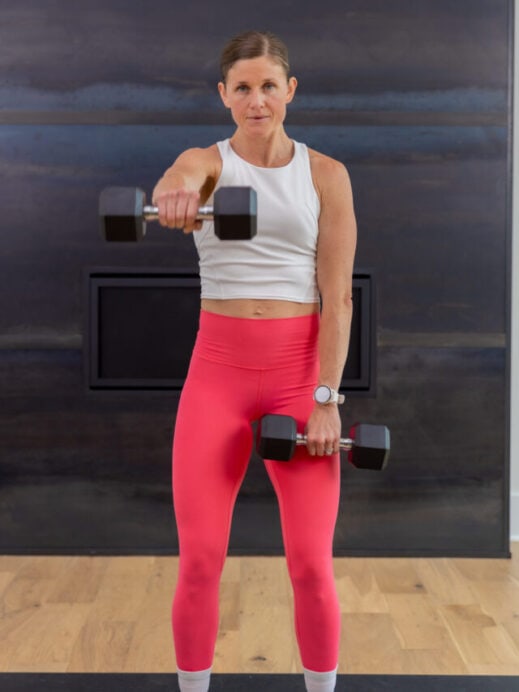 woman performing a single arm front raise in an arm workout with dumbbells