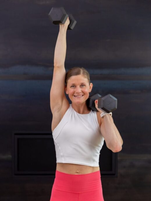 woman performing a single arm overhead press with dumbbells in an upper body workout