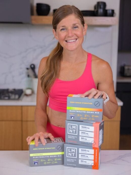 woman standing in her kitchen next to several boxes of LMNT electrolyte drink mix | muscle recovery supplements