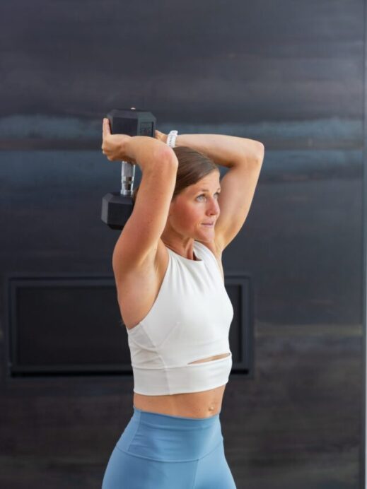 woman performing an overhead tricep extension with a dumbbell in a tricep workout