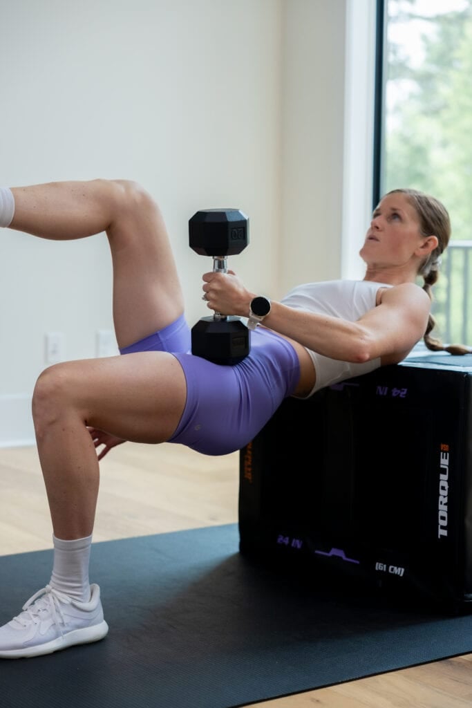 woman performing a single leg glute bridge with a dumbbell as part of dumbbell leg workout