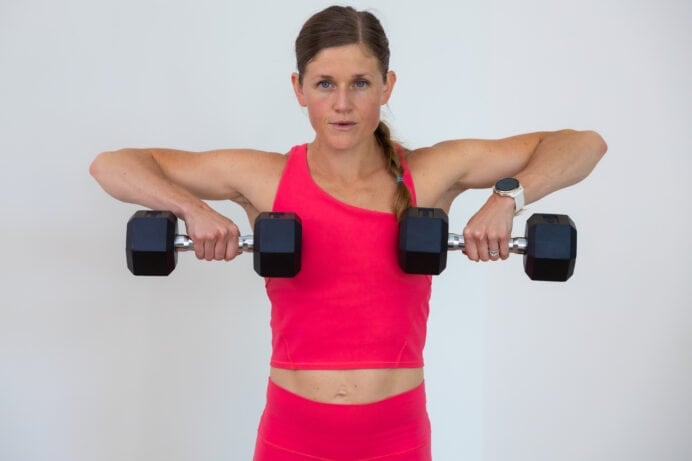 woman performing a dumbbell front raise as part of dumbbell shoulder workout