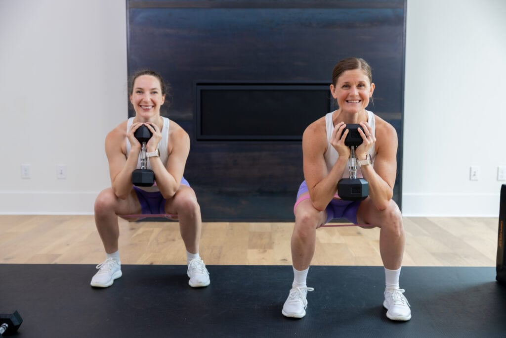 two women performing a goblet squat with dumbbells as part of dumbbell leg workout