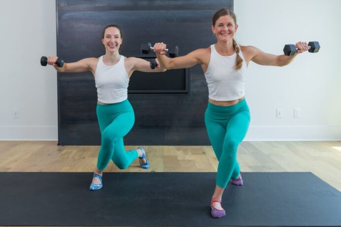 two women performing a curtsy lunge and l-fly with light weights in a barre workout at home