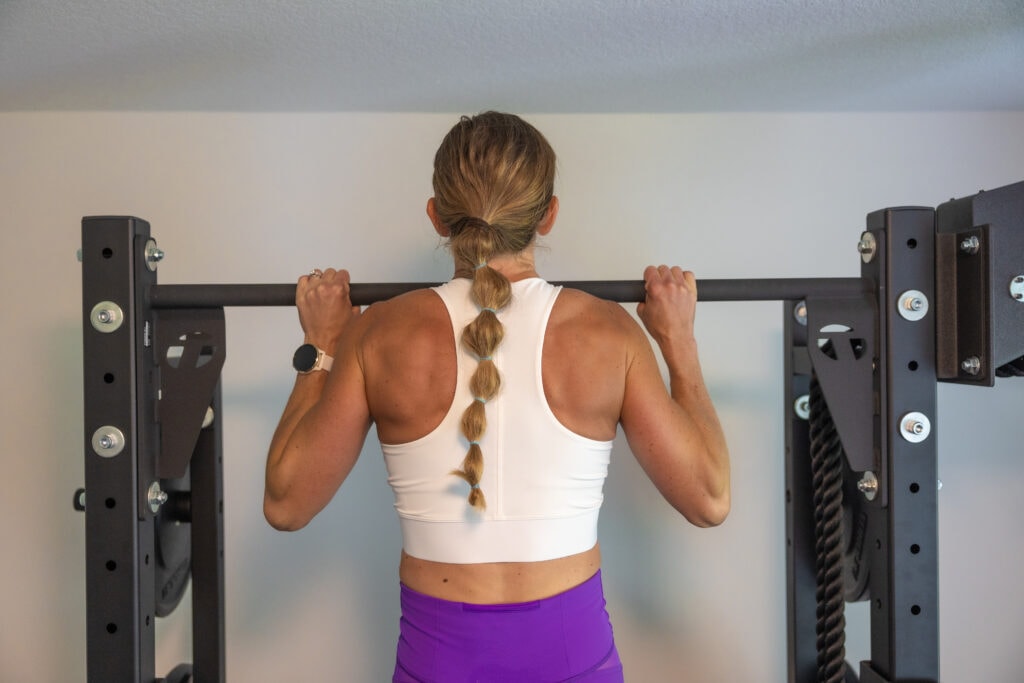 Woman doing pull ups on a bar with her hands shoulder width apart and shoulder blades activated. How to do a pull up. 