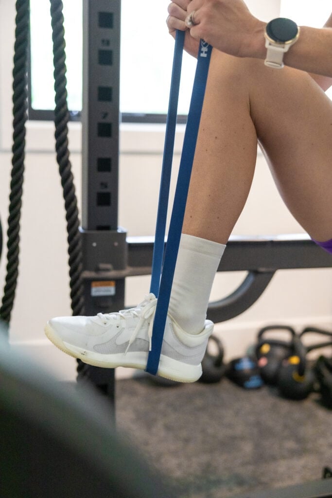 Women putting her foot through a long resistance band to show how to do a resistance band pull up at home.