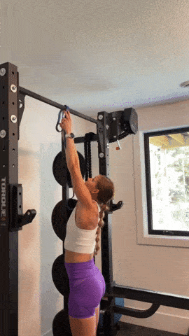 Woman putting a long loop resistance band onto a pull up bar and looping the band through her foot to show how to do an assisted pull up with a resistance band. Using upper body strength to work towards a full pull up.