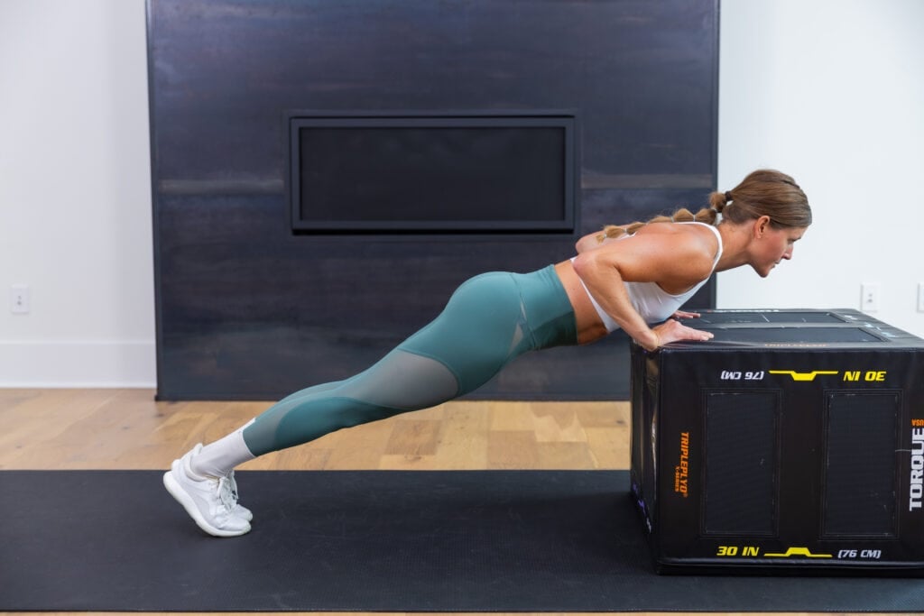 Women performing an elevated push up from an incline using a box with arms shoulder width apart. To show a modification for a push up progression in 12 weeks. 