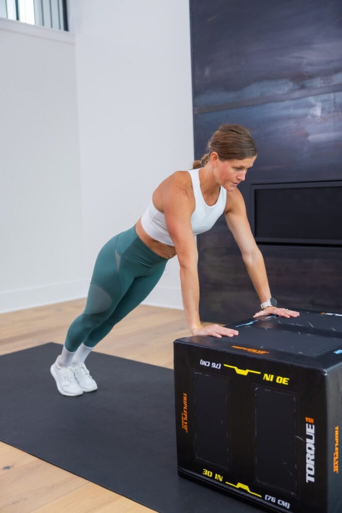 Women setting up for an incline push up in a high plank during an elevated push up progression guide. 