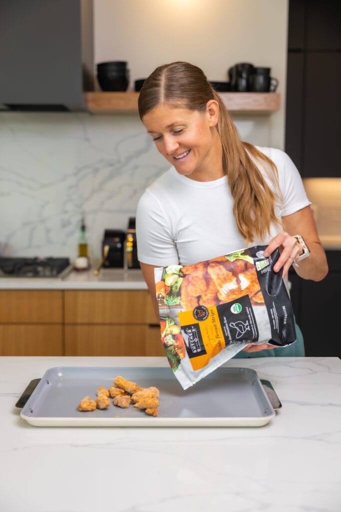 Women in her kitchen meal prepping a sheet pan dinner for roasting vegetables and chicken, using her stainless steel caraway large sheet pan. Kitchen Essentials.