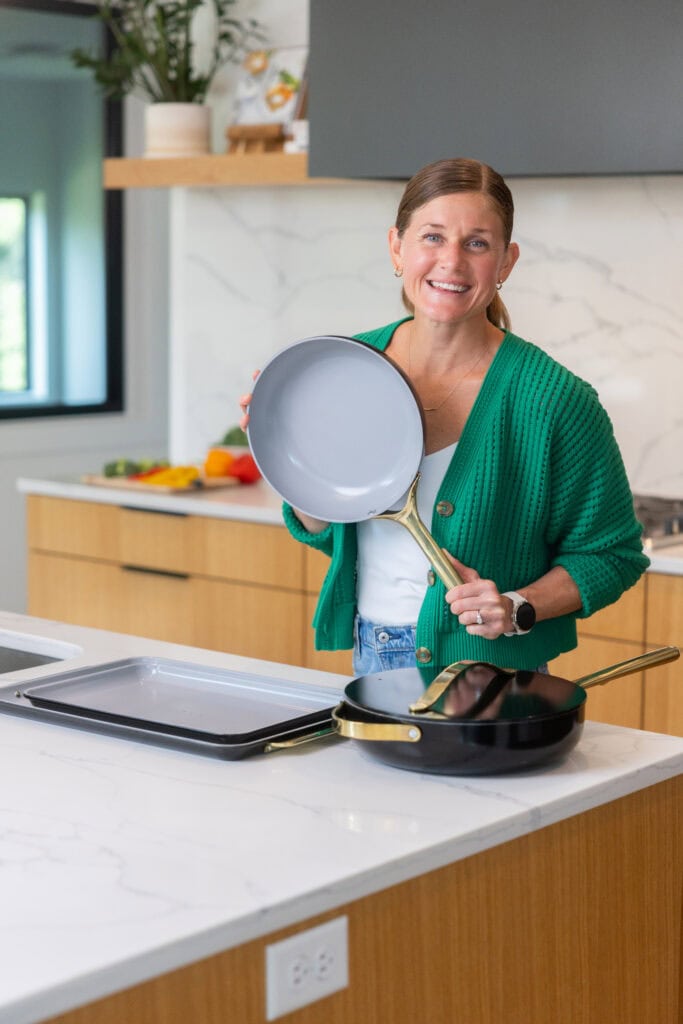 Women with Caraway cookware set all set up in a white kitchen next to stove.