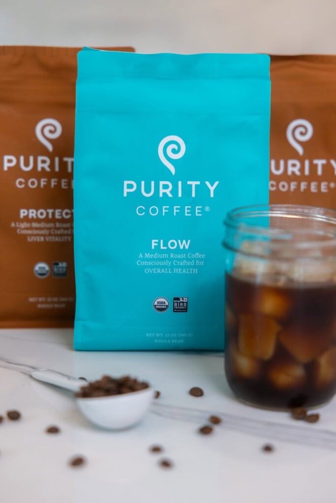 three bags of Purity Coffee grounds and cup of purity cold brew.