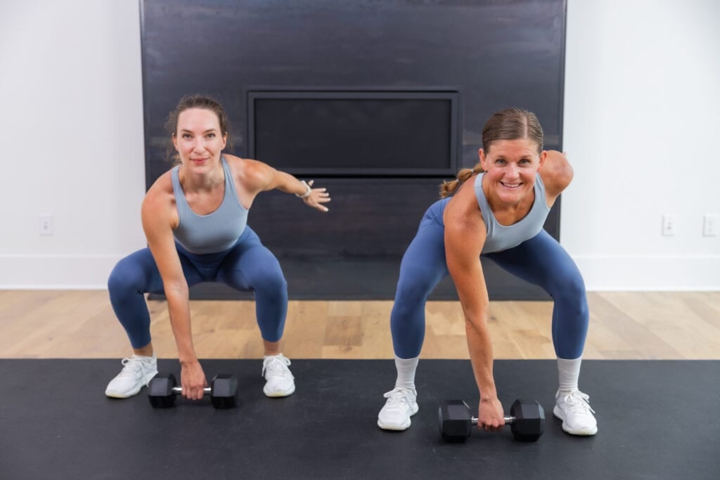 two women holding the bottom of a squat preparing to perform a dumbbell snatch in a total body workout