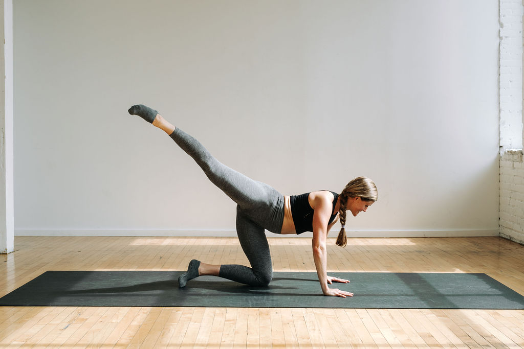 woman performing a table top leg lift as part of cardio barre burn workout class