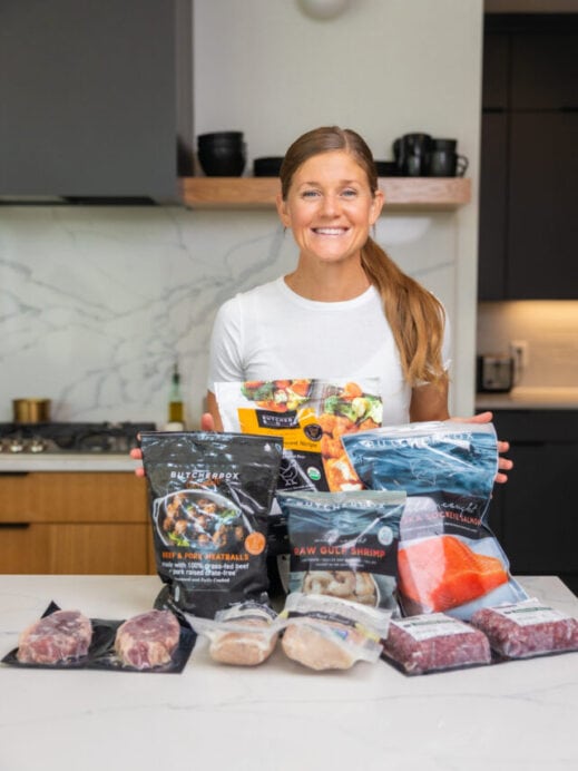 Woman standing in her kitchen with meat and seafood from a ButcherBox delivery