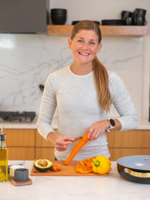 Woman peeling a carrot and meal prepping in her kitchen using her kitchen essentials.