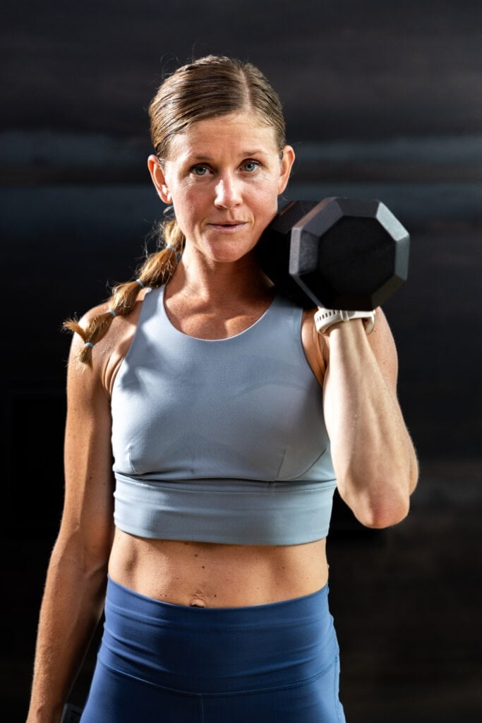 woman holding a single dumbbell racked at her shoulder in a full body squat thruster workout